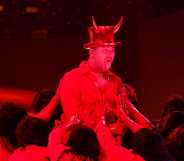 A screenshot from the 2023 Grammys ceremony shows Sam Smith performing "Unholy" on stage wearing a hat showing devil horns as a red spotlight casts a strong red light over him