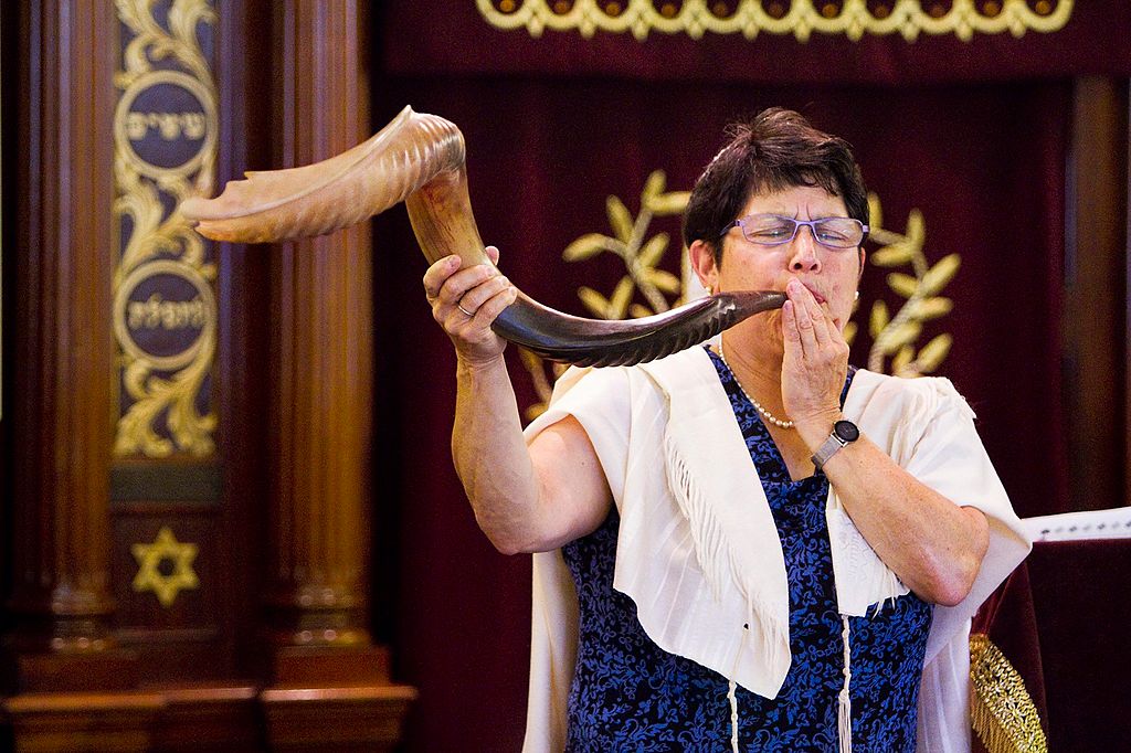 A woman rabbi holding a shofar, a long curved horn, to her mouth