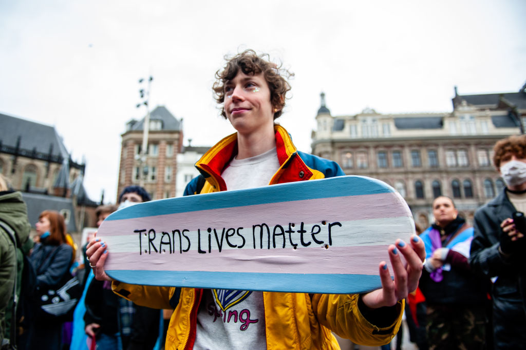 A person is holding a skateboard with the colors of the transgender flag and with a message in support of trans people.