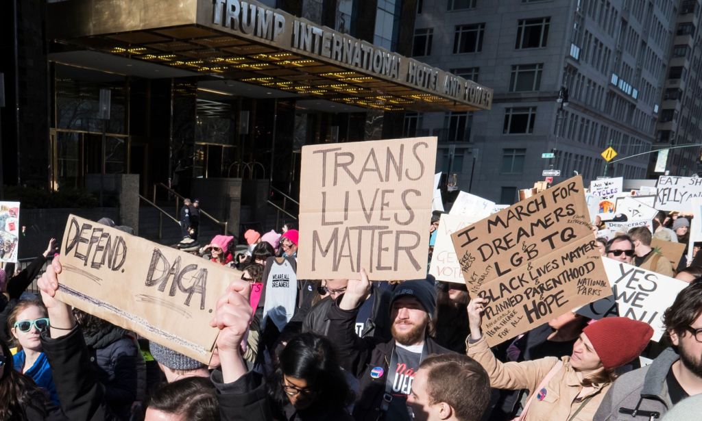 One person holds up a sign reading 'Trans lives matters' while others hold up signs in support of the LGBTQ+ community during a rally against Republican president Donald Trump