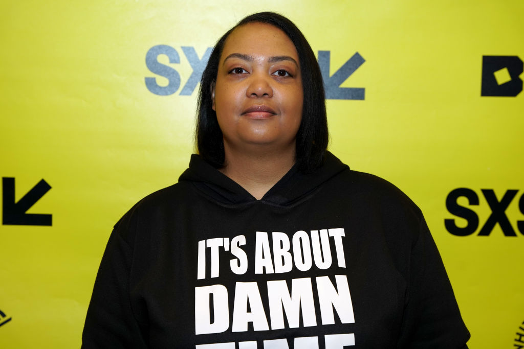 Arlan Hamilton poses for the camera. She is wearing a hooded sweatshirt with the words "It's About Damn Time"