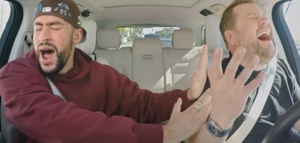 Bad Bunny and James Corden singing and gesturing passionately in the front of a car