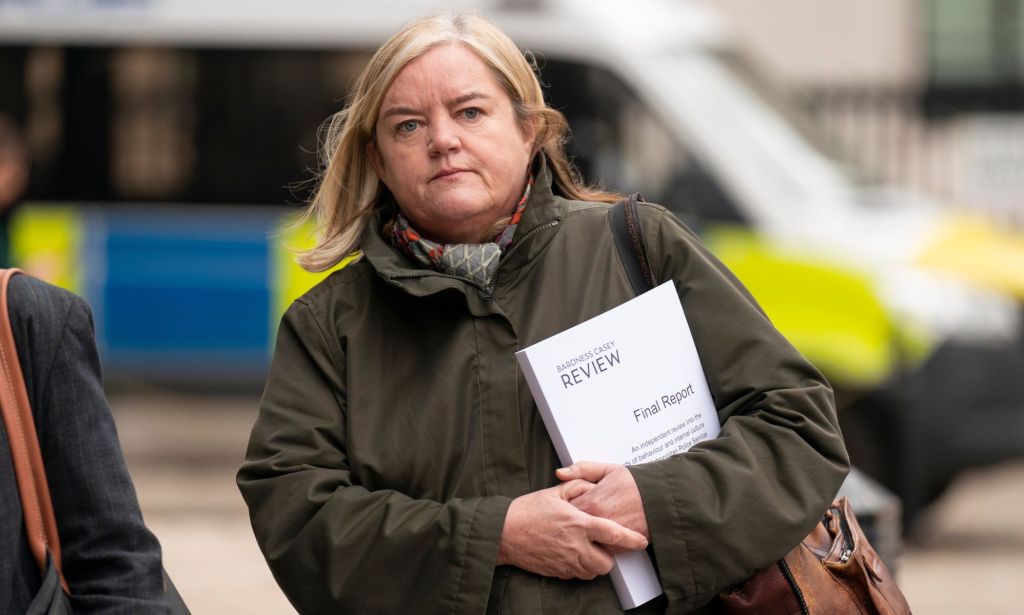 Baroness Casey walking across a street holding a copy of her final Met police report.