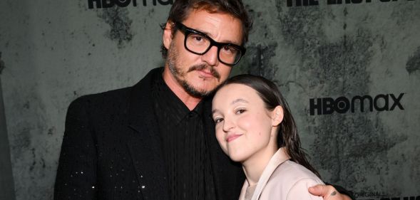 Pedro Pascal in a black suit and black glasses hugging Bella Ramsey, who is smiling and wearing a light pink suit.