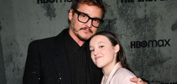 Pedro Pascal in a black suit and black glasses hugging Bella Ramsey, who is smiling and wearing a light pink suit.