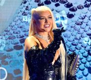 Christina Aguilera in a blue dress holding a microphone and her GLAAD Award stood against a blue sequinned background.