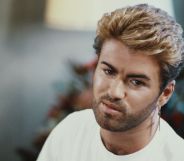 George Michael in a room wearing a white t-shirt, looking to the side of the camera.