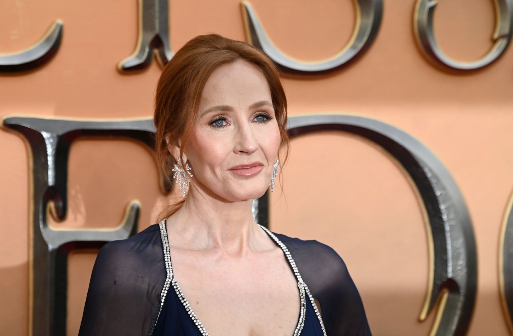 JK Rowling wears a navy blue dress against an orange background at a film premiere