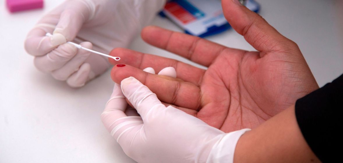 An image shows a person having a HIV test with a blood prick on their finger.