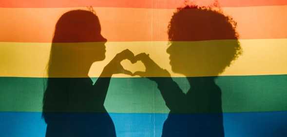 People making a heart shape behind a pride flag