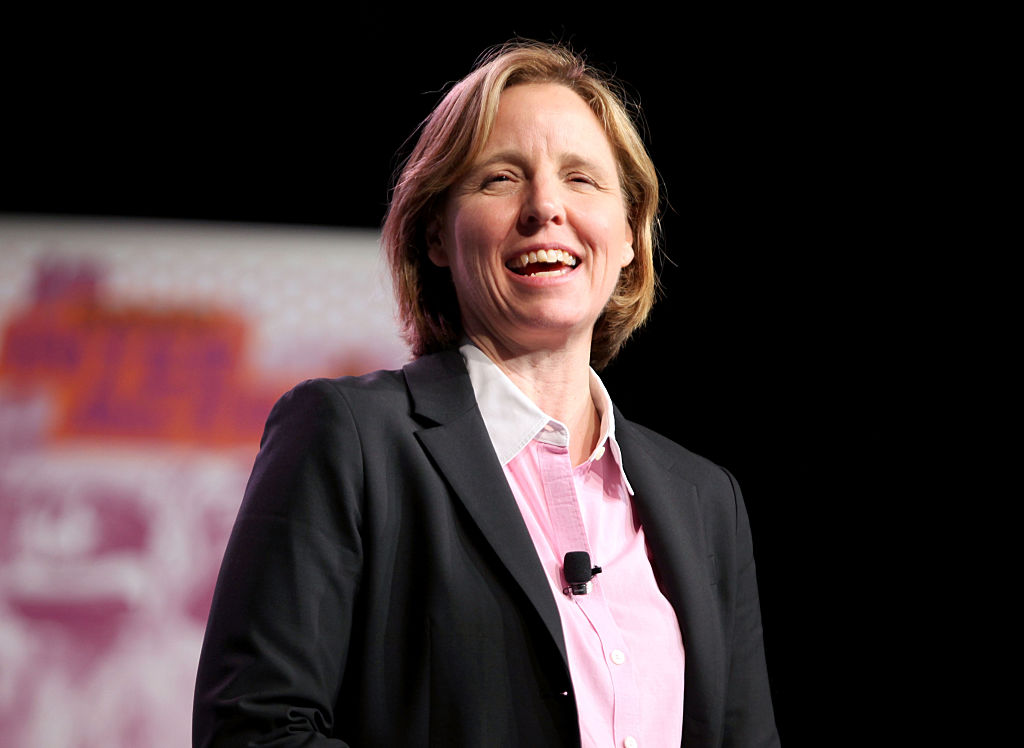 Megan smith is onstage speaking at a conference. She is wearing a black blazer with a pink shirt.