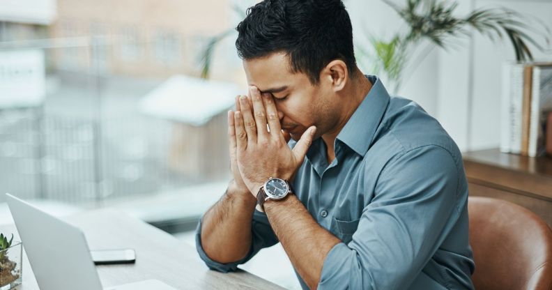 A man is wearing a blue shirt with the sleeves rolled up to his elbow. He appears stressed as he has his hands in his face.