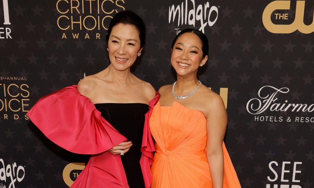 Michelle Yeoh wearing a pink and black dress, smiling and stood next Stephanie Hsu, wearing an orange dress, at the Critics Choice Awards.
