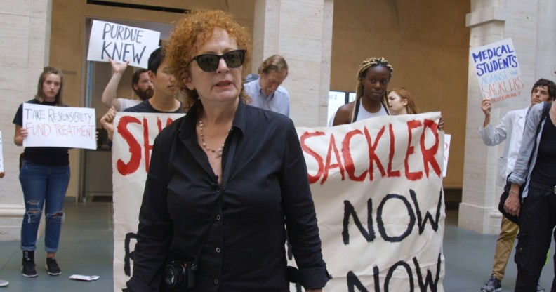 Nan Goldin at a protest, stood in front of banners