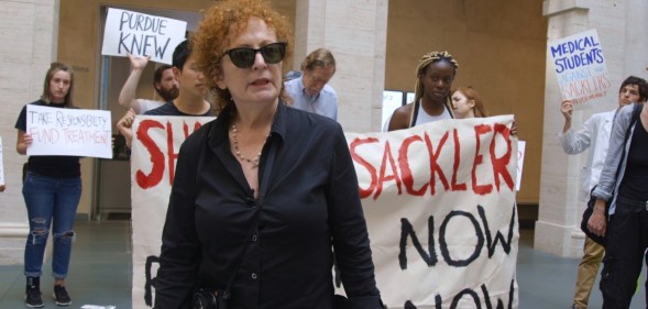 Nan Goldin at a protest, stood in front of banners