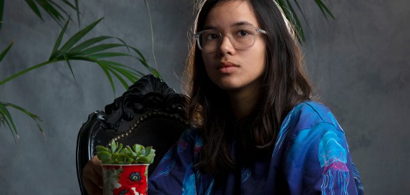 Pippa sitting, holding a potted succulent on their knee