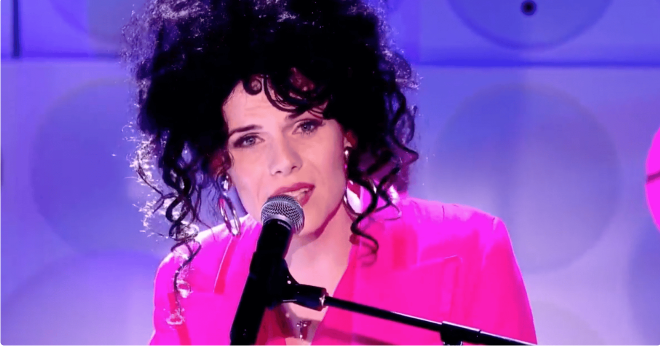 Jordan Gray wears a pink suit as she sings into a microphone during her live performance on Channel 4 Friday Night