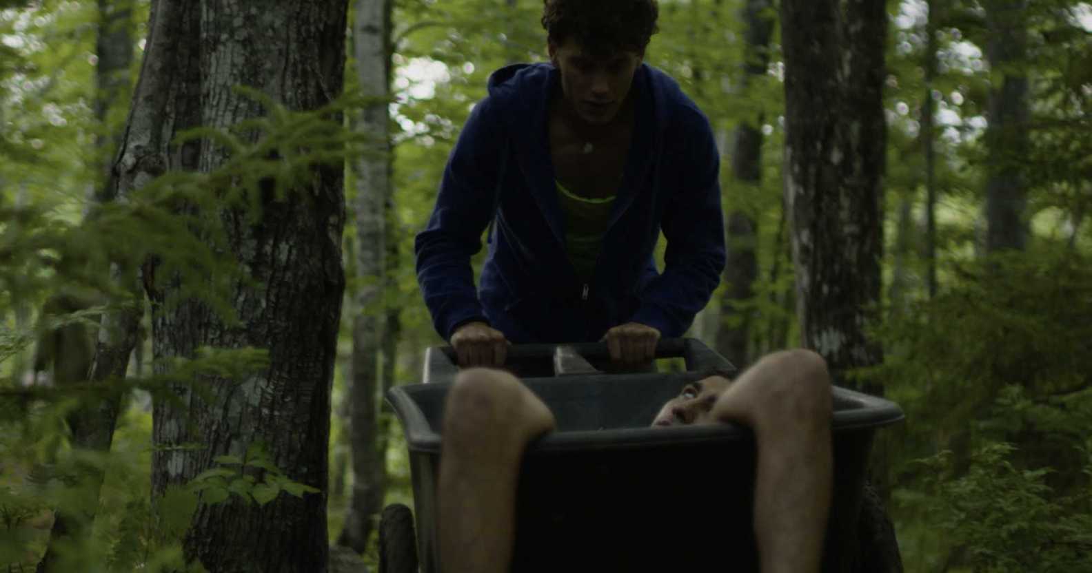A man pushes a wheelbarrow with a body in.