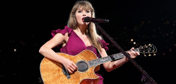 Taylor Swift in a dark pink gown singing with her guitar on the Eras Tour.
