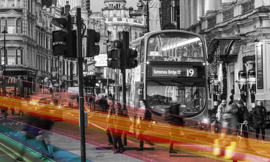 A black and white picture of a TfL bus in London with rainbow Pride colours superimposed across the road