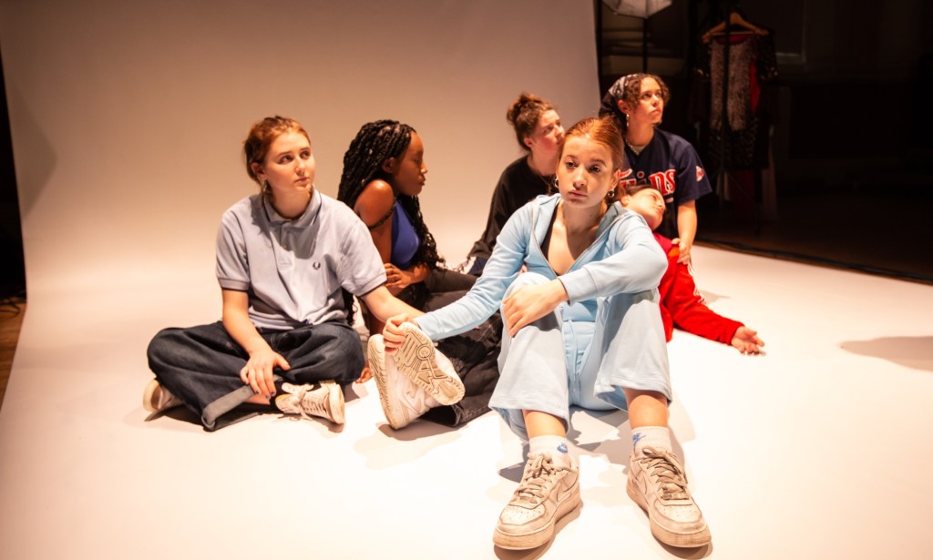 The cast of Charlie Josephine's Flies sitting on the floor in a circle looking stoic.