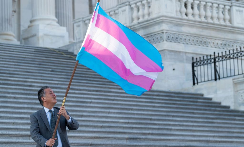 US congressman Mark Takano holds up a trans Pride flags on the steps of a building