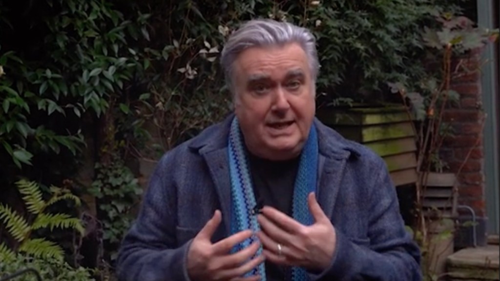 SNP politician John Nicholson sits in a garden wearing a blue jacket.