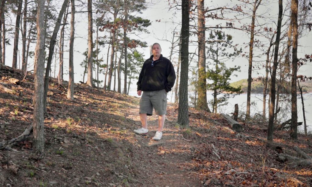 Wayne Maines stands in the woods, looking at the camera.