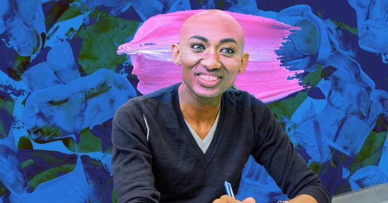 A trans person is smiling for the camera. They are bald, and wearhing a grey v-neck shirt with the sleeves rolled up to their elbows.