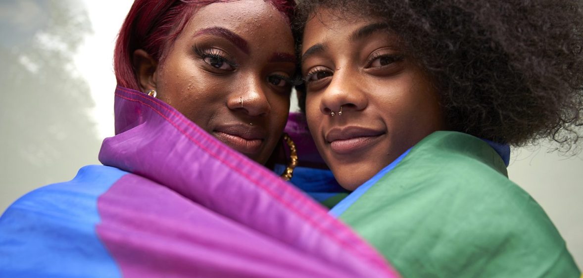 Two women draped in a rainbow Pride flag.