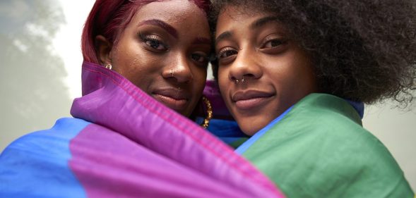 Two women draped in a rainbow Pride flag.