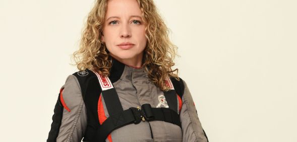 Queer stunt driver and professional drift driver Zandara Kennedy wears a grey, black and red motorsports outfit as she poses for the camera