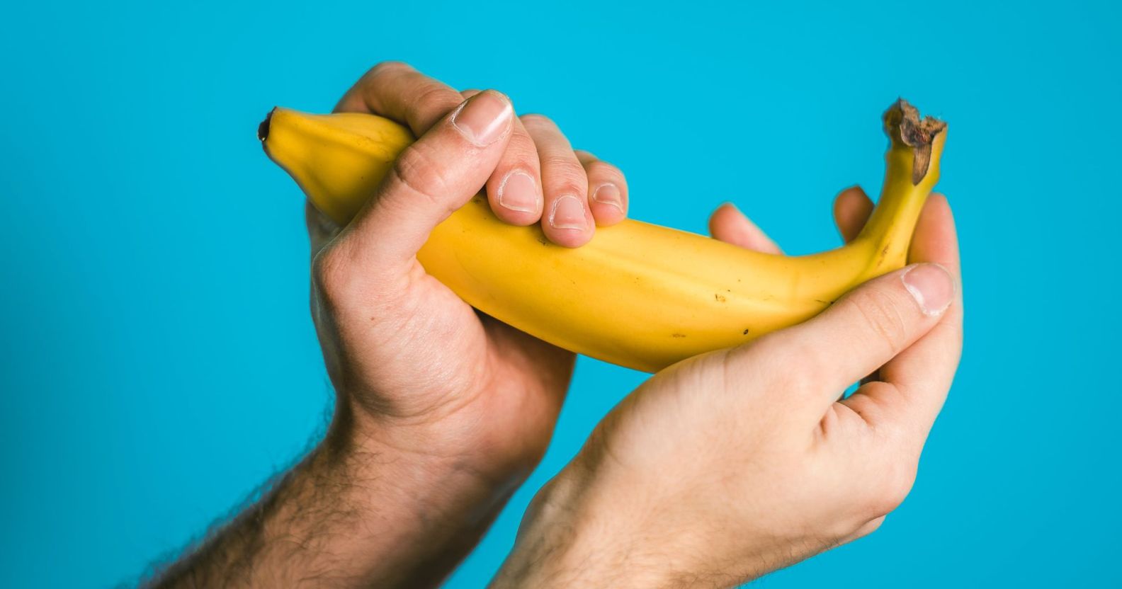 A person is holding a yellow banana in both hands against a light blue background