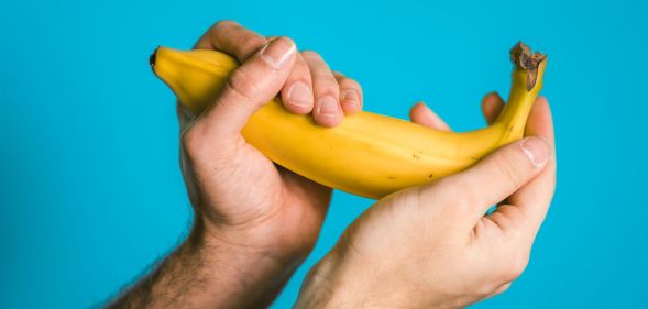 A person holds a yellow banana in both hands in front of a light blue background