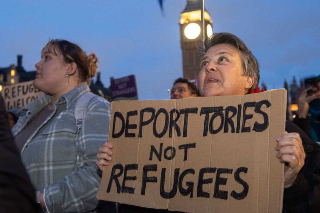 Hundreds of people protested in Parliament Square against the Illegal Migration Bill. A person is pictured holding a sign which says "deport Tories not refugees".