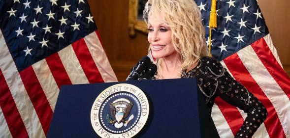 Dolly Parton behind a podium with the presidential seal. The US flag hangs behind her