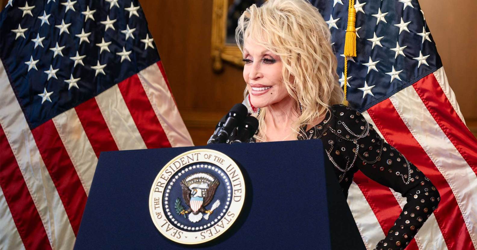 Dolly Parton behind a podium with the presidential seal. The US flag hangs behind her