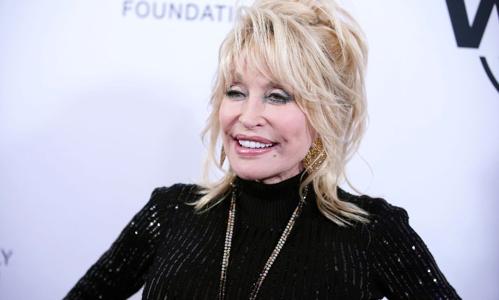 Dolly Parton pictured on the red carpet wearing a black dress and a gold chain.