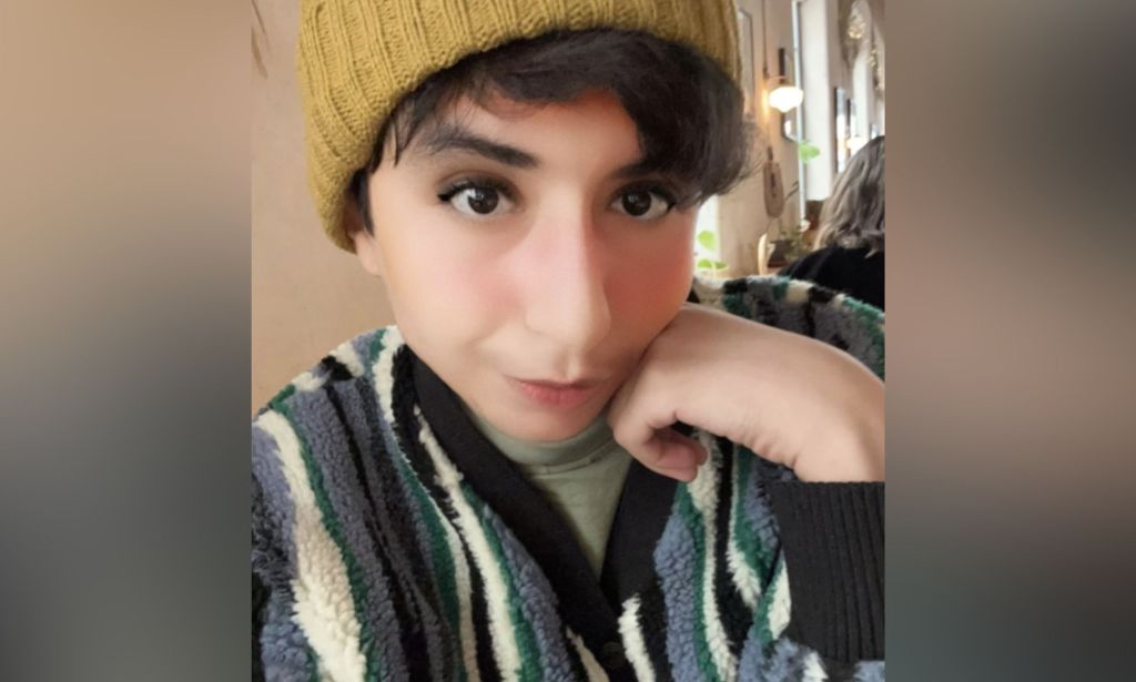 Eden Knight, a young Saudi trans woman, wears a vertical striped jumper in black, cream and grey with a yellow beanie hat