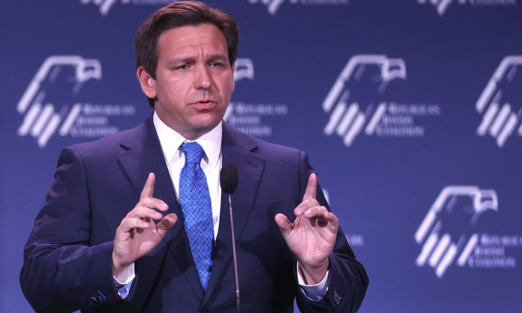 Florida governor Ron DeSantis wears a suit and tie as he gestures with one finger raised upwards on both hands during a speech