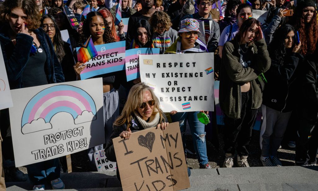 A crowd of people, many of whom are young, hold up signs in support of the LGBTQ+ community and trans youth as they protest the passing of SB 150 at the Kentucky state capitol.