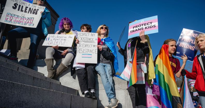 A crowd of people hold up LGBTQ+ and trans Pride flags as well as signs in support of the community as they sit on the Kentucky state capitol steps to protest against the passing of SB 150