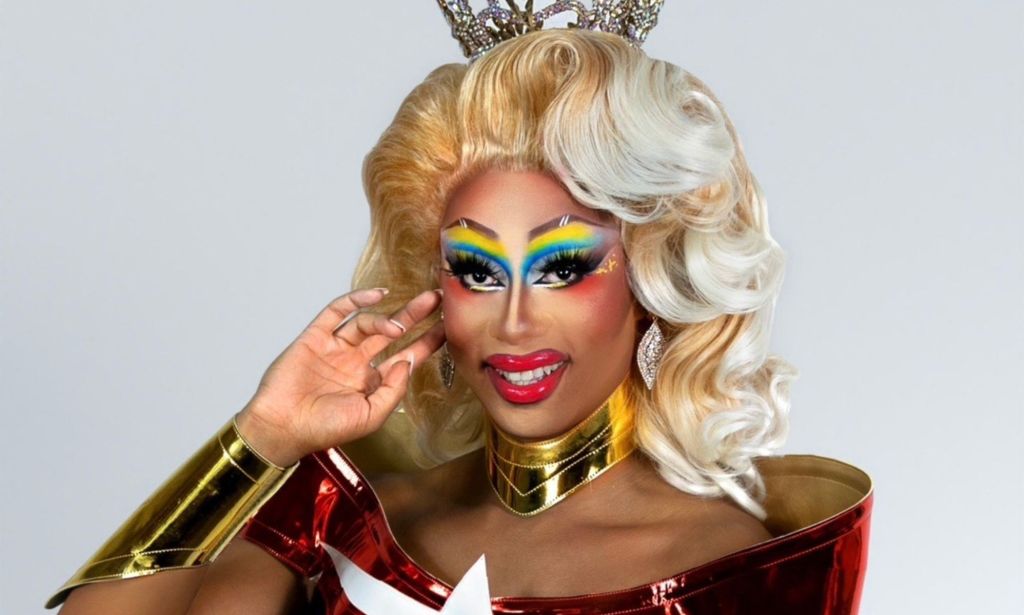 Texas-based drag queen Kylee Ohara Fatale poses with one arm raised up towards her face while wearing a red white and blue outfit and rainbow eye makeup