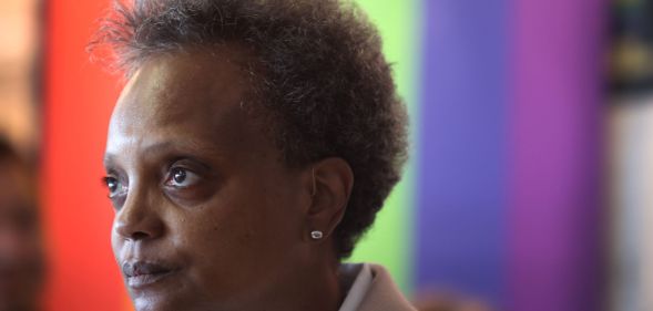 Chicago mayor Lori Lightfoot stands in front of a rainbow LGBTQ+ pride background as she stares somewhere off camera
