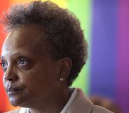Chicago mayor Lori Lightfoot stands in front of a rainbow LGBTQ+ pride background as she stares somewhere off camera