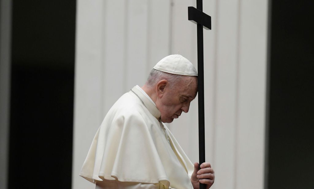 Pope Francis wears a white garments as he holds up a dark coloured cross