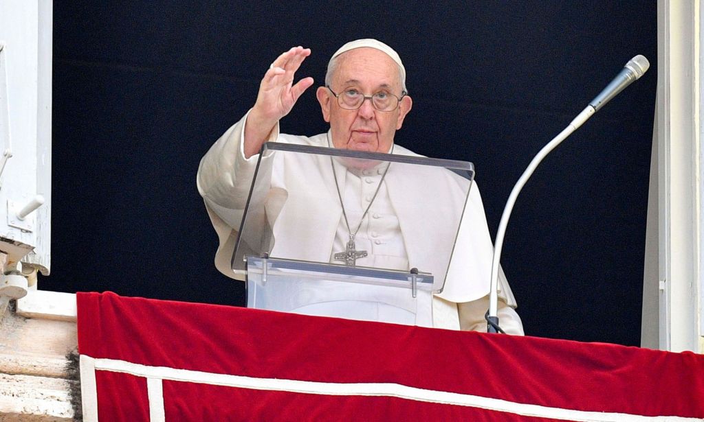 Pope Francis wears a white jacket, white robes and cap as he waves from a balcony to people gathered in a public audience at the Vatican in Rome