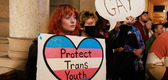Protesters hold a placard that says, "Protect trans youth" and "Gay" as they protest against Republicans attacking LGBTQ+ rights including education on queer topics and trans healthcare