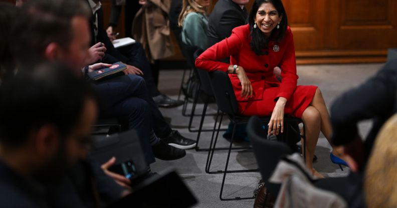 Suella Braverman sitting in a chair, laughing with people surrounding her