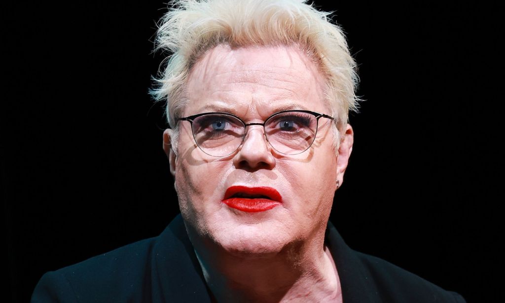 Trans actor Suzy Eddie Izzard wears dark clothing as she sits in front of a dark background